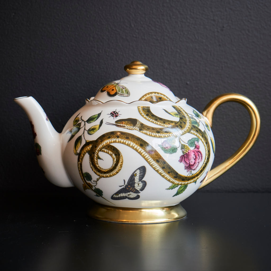 Ceramic teapot with floral and snake design on a light background. Gold handle.