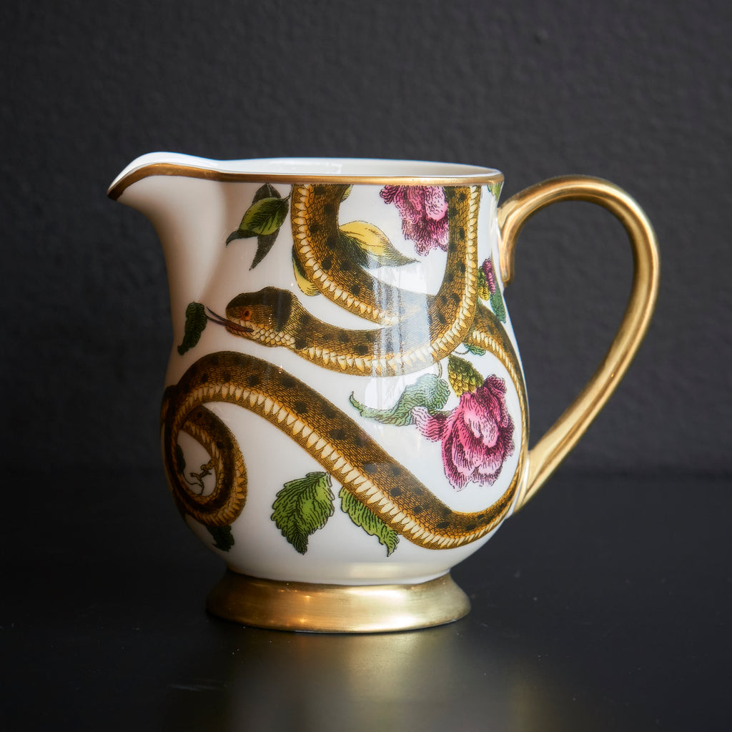 Ceramic creamer pitcher with snake and floral design on a light background